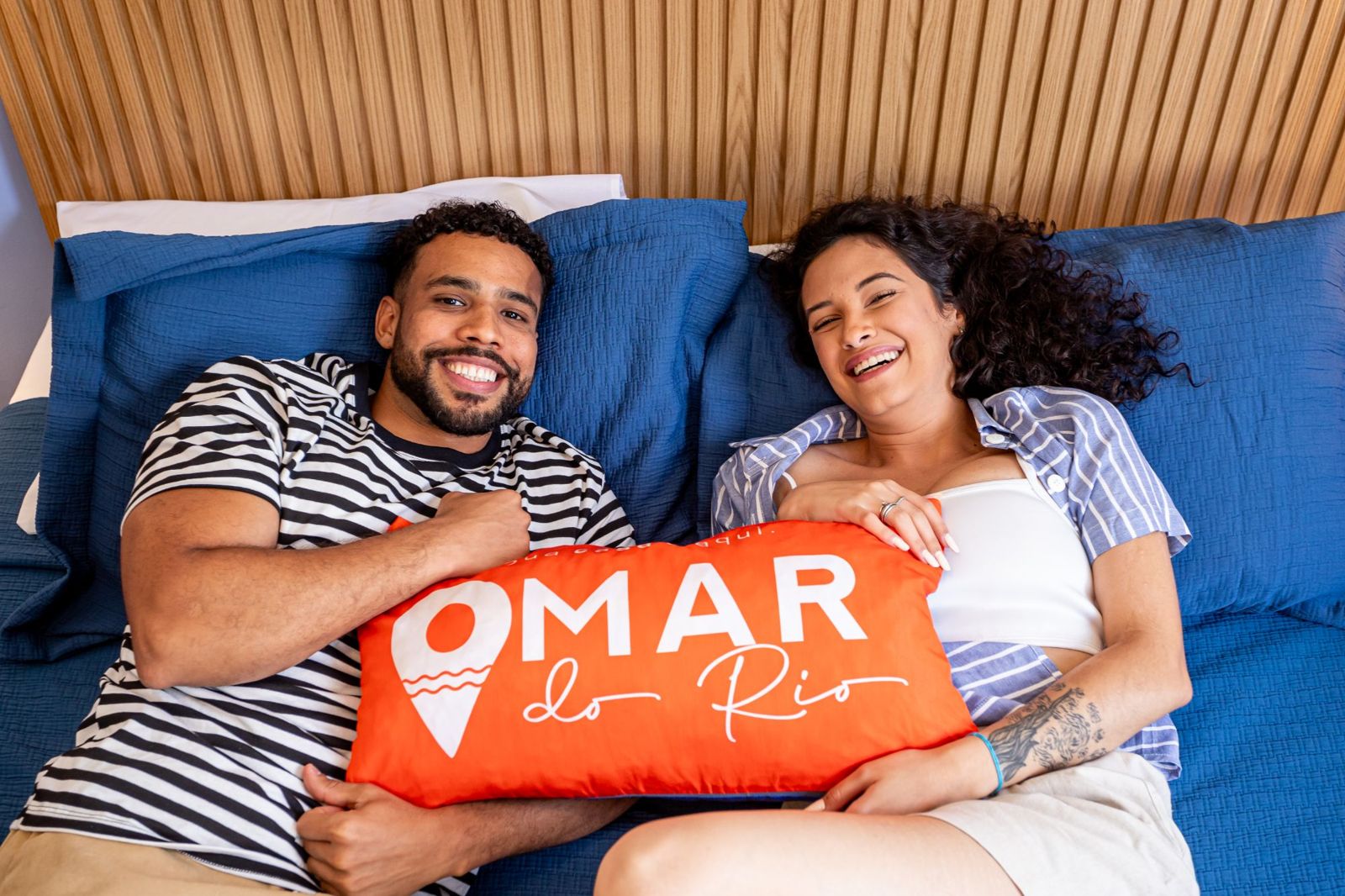 Casal sorrindo com a almofada da Omar do Rio em um apartamento